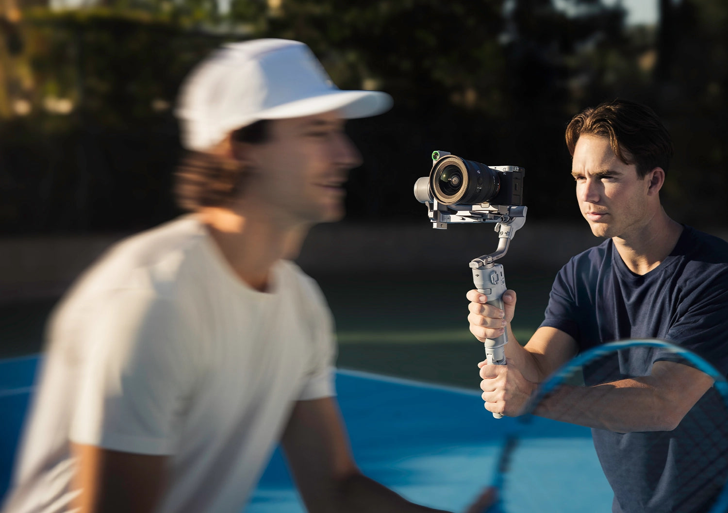 A man filming a tennis player using a DJI RS 4 Mini